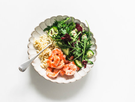 Delicious lunch - risoni pasta, shrimp and arugula, cucumber, celery salad on a light background, top viewの写真素材