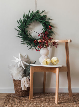 Christmas composition - a basket with blankets, Scandinavian stars, a Christmas wreath on the wall, a vase with cranberry branches on a chair. Scandinavian style interiorの写真素材