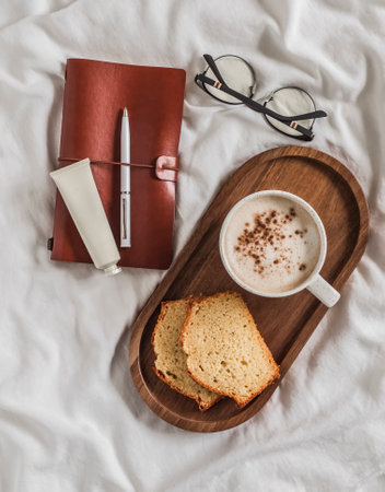 A cozy morning - a cup of coffee, pieces of cupcake on a wooden tray, a notebook, hand cream,...
