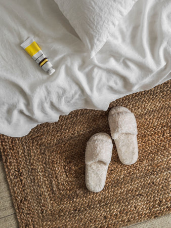 Hand cream on the white sheets of the bed, slippers. Cozy home conceptの写真素材