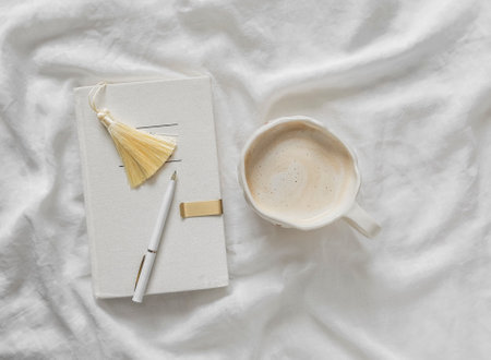 Lazy morning - personal diary with decorative brush bookmark, cappuccino cup in bed, top view