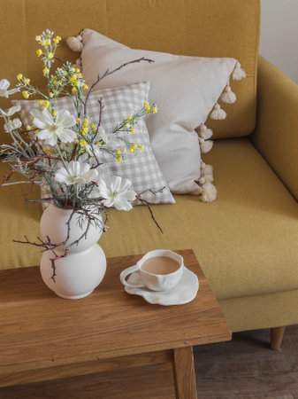 A cup of tea with milk, a vase of flowers on a wooden table next to a yellow armchairの写真素材