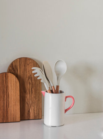 Kitchen appliances in a ceramic jug, wooden cutting boards on the kitchen tableの写真素材