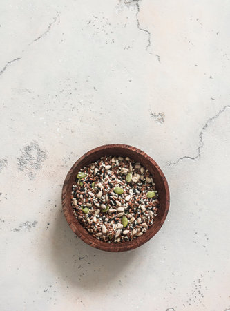 A mixture of seeds for salad, smoothies, sandwiches - white black sesame seeds, flaxseeds, pumpkin seeds, sunflower seeds in a wooden bowl on a light backgroundの写真素材
