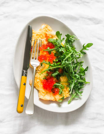 Cheese omelet with red caviar and arugula on a light background, top view