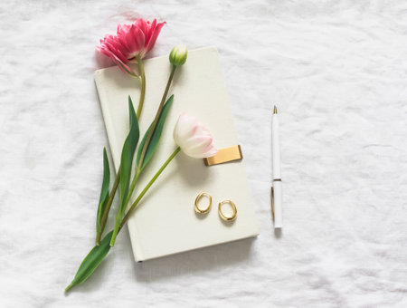 Tulips, a book, earrings, a pen on white sheets top view. Aesthetic still lifeの写真素材