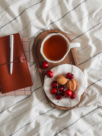Aesthetics of the morning - a cup of tea, sweets, cherries, a notebook on linen bed linen, top viewの写真素材