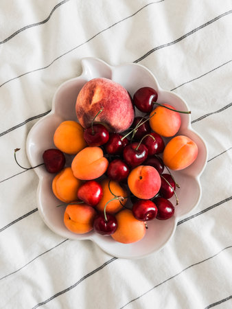 Ceramic bowl with fresh juicy fruits - apricots, peaches, cherries on a light background, top view