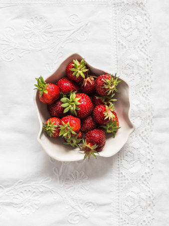 Fresh ripe strawberries in a ceramic bowl on a light background, top viewの写真素材
