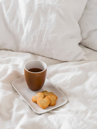 Coffee and cookies hearts on a white ceramic tray on white sheets in bedの写真素材