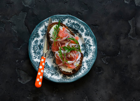 Lightly salted salmon, cottage cheese, arugula, onion, rye bread sandwich on a vintage plate on a dark surfaceの写真素材