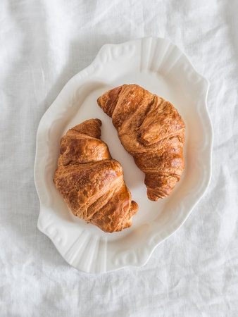 Fresh homemade croissants on a white plate on a light surfaceの写真素材
