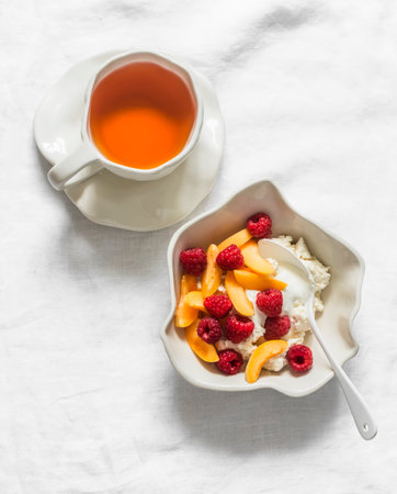 Delicious breakfast - cottage cheese with raspberries and apricots, a cup of tea on a light surface, top viewの写真素材