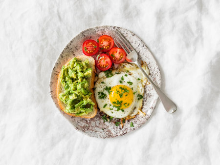 Delicious breakfast, snack, brunch - fried egg, cherry tomatoes and avocado sandwich on a light surface, top viewの写真素材
