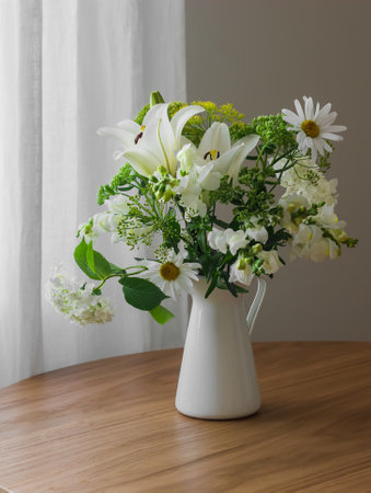 A bouquet of summer flowers in a metal jug on a round wooden table in the living roomの写真素材