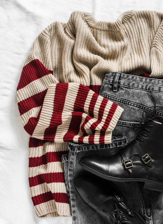 Women's autumn spring clothing - beige sweater with burgundy stripes, black jeans, leather boots on a light background, top viewの写真素材