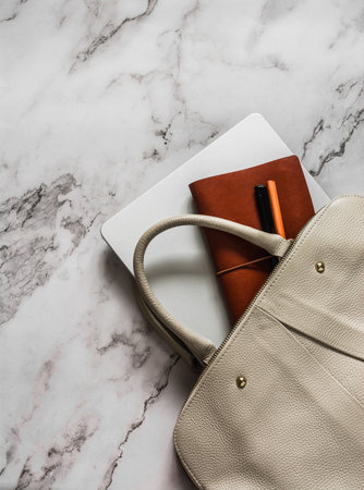 Women's beige leather bag, laptop, notebook, pen on marble background, top viewの写真素材