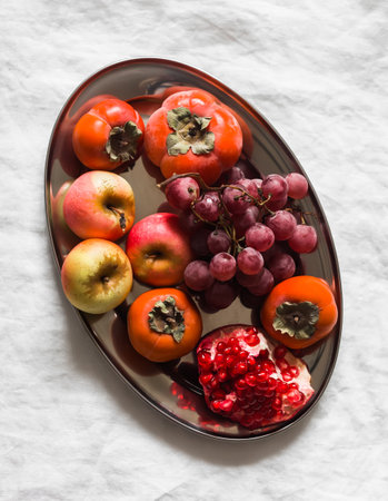 Seasonal fruits - persimmon, red grapes, apples, pomegranate on a light background, top view
