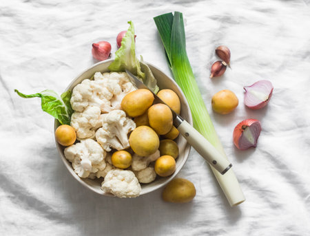 Ingredients for cooking lunch - potatoes, cauliflower, leeks, red onion, garlic on a light background, top viewの写真素材