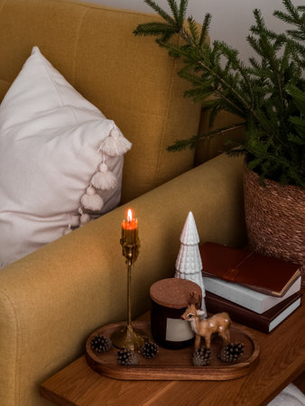 Christmas decor, candles, fir branches in a basket on a wooden table next to a yellow armchairの写真素材