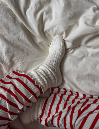 A woman in red striped pajama pants and warm socks is sitting on a bed, top viewの写真素材