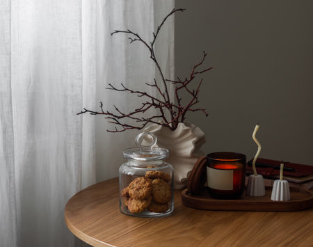 Cozy autumn mood house - a jar of oatmeal cookies, an autumn bouquet, candles on a round wooden table in the living roomの写真素材