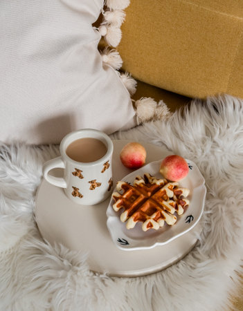 Coffee with milk, waffles, nectarines on a fluffy cozy blanket on a yellow sofa. Autumn moodの写真素材