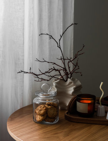 A cozy autumn composition on a round wooden table - a cookie jar, an autumn foliage bouquet, lighted candles. Cozy home conceptの写真素材