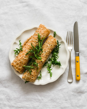 Crepes stuffed with tuna, cucumber, eggs, arugula salad on a light background, top view