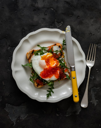 Whole grain bread sandwich with poached egg, arugula and red caviar on a dark background, top view. Delicious breakfastの写真素材