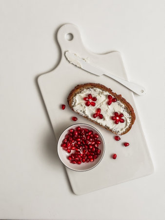 Creative sandwich with cottage cheese and pomegranate on a white ceramic board on a light background