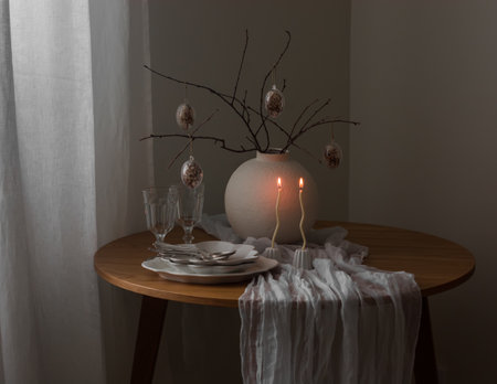Easter bouquet with eggs decor in a ceramic vase, candles, dishes on a round wooden tableの写真素材
