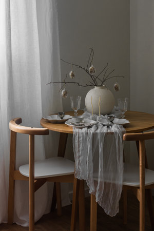 Festive Easter setting - Easter bouquet in a ceramic vase, dishes on a round wooden table in the living roomの写真素材