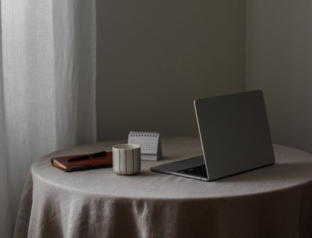 A laptop, a notebook, a glass of coffee on a round table with a gray tableclothの写真素材