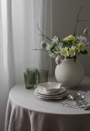 Easter table setting - plates, glasses, cutlery, Easter flower arrangement on a round table in the living room.の写真素材