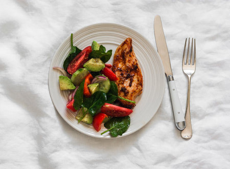 Baked chicken breast and fresh avocado, tomatoes, peppers, spinach salad - a delicious diet lunch on a light background, top viewの写真素材