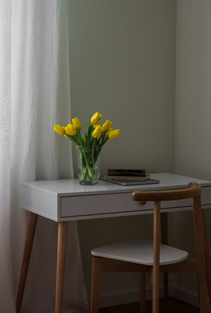 A cozy workplace - a bouquet of yellow tulips, a laptop, a notebook on a white tableの写真素材