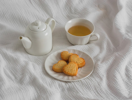 A cup of green tea, shortbread cookies in the shape of a heart, a teapot on a light backgroundの写真素材