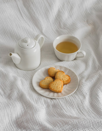 A cup of green tea, shortbread cookies in the shape of a heart, a teapot on a light backgroundの写真素材