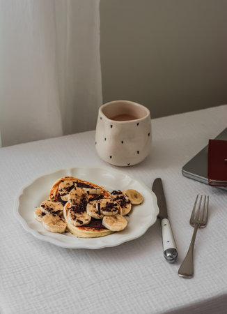 Pancakes with banana and chocolate and coffee with milk on the table - delicious breakfast, dessert, snackの写真素材