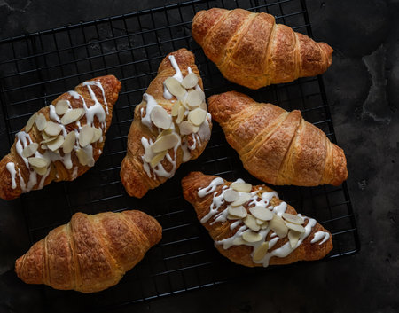 Freshly baked croissants with icing sugar and almond petals on a dark background, top viewの写真素材