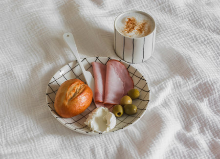 Delicious breakfast - ham, roll, cheese, olives on a plate on a light backgroundの写真素材