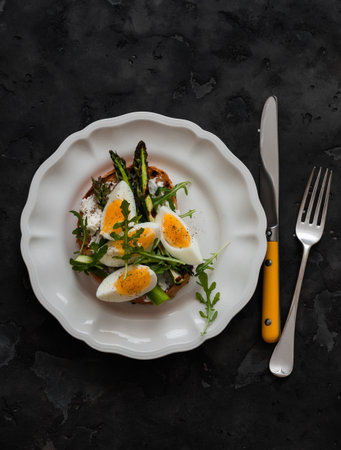 Sandwich with cottage cheese, grilled asparagus, boiled egg - delicious breakfast, snack, tapas on a dark background, top viewの写真素材