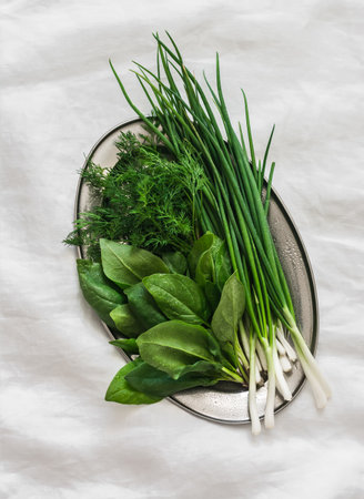 Fresh green onions, spinach, dill on a metal dish on a light background, top viewの写真素材