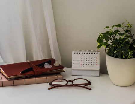 Notebooks, house flower, glasses, calendar on the white table in the bedroomの写真素材