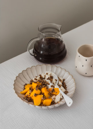 Delicious homemade breakfast - cottage cheese with Greek yogurt, fresh mango, granola and black coffee on the tableの写真素材