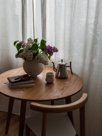 A bouquet of lilacs in a vase, a glass, a coffee pot, books on a round wooden table in the living roomの写真素材