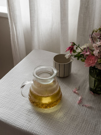 Buckwheat tea in a glass teapot on a table with a white tablecloth and a bouquet of wildflowersの写真素材