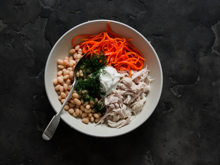 The idea of the salad - canned beans, boiled chicken fillet, spicy carrots, natural yogurt and dill in a bowl on a dark background, top viewの写真素材