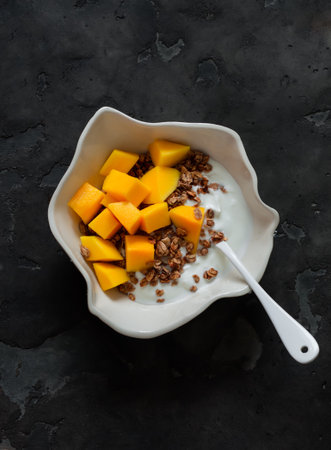 Delicious breakfast - Greek yogurt, crispy granola, fresh mango in a bowl on a dark background, top viewの写真素材